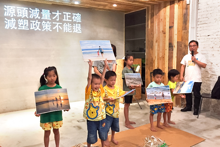 純真的孩童，手持美麗海景照片與塑膠垃圾製成的「海廢浮世繪」共同合照